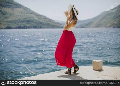 Young attractive woman with a hat poses by the sea in the summer