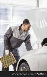 Young automobile mechanic examining car in automobile shop