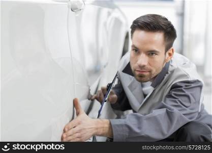 Young automobile mechanic examining car in repair store