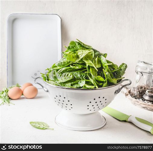 Young baby spinach in white colander on white kitchen table with eggs. Tasty healthy food.