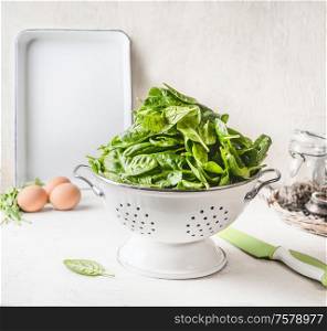 Young baby spinach in white colander on white kitchen table with eggs. Tasty healthy food.