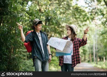 Young backpacker couple wearing hat and holding paper map are arguing about direction of forest trail.
