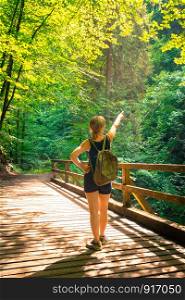 Young backpacking girl is staying on a wooden bridge in an idyllic forest and is enjoying the view
