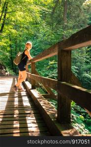 Young backpacking girl is staying on a wooden bridge in an idyllic forest and is enjoying the view