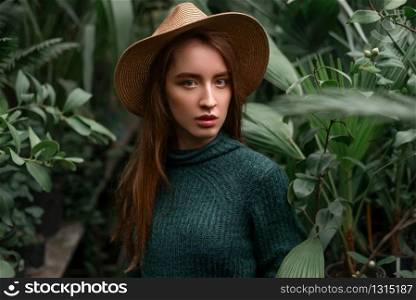 Young baeutiful woman standing at nursery in a greenhouse.