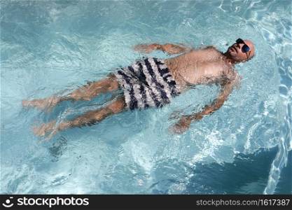 Young bald handsome male floating in a swimming pool wearing sunglasses