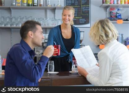 young barista serving coffee to a couple in cafe