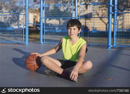 Young basketball player sitting on the court wearing a yellow sleeveless