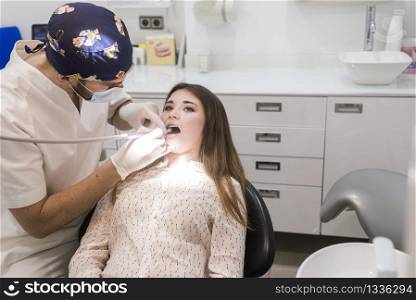 Young bearded dentist drilling tooth to female patient.