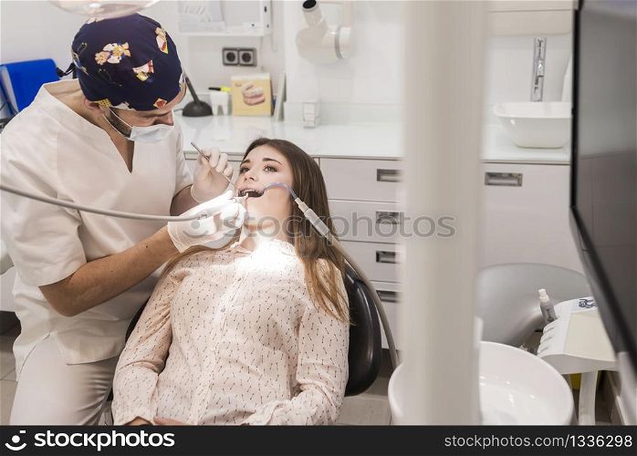 Young bearded dentist drilling tooth to female patient.