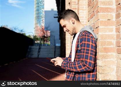 Young bearded man leaning on a bricked wall while using a smartphone