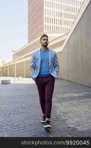 Young bearded man, model of fashion, in urban background wearing casual clothes while walking with hands on pocket