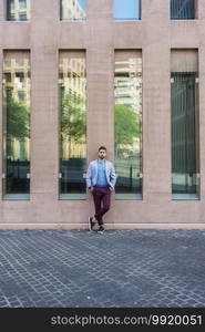 Young bearded man, model of fashion, in urban background wearing casual clothes while leaning on a office building wall