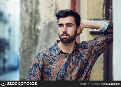 Young bearded man, model of fashion, wearing modern shirt in the street. Guy with beard and modern hairstyle in urban background.