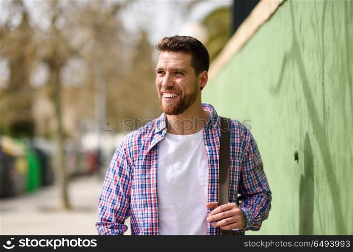 Young bearded man smiling in urban background. Lifestyle concept. Young bearded man smiling in urban background. Traveler wearing casual clothes. Lifestyle concept.
