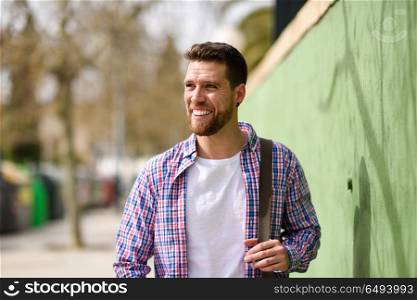Young bearded man smiling in urban background. Lifestyle concept. Young bearded man smiling in urban background. Traveler wearing casual clothes. Lifestyle concept.