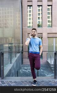 Young bearded man standing in the street while talking by mobile phone