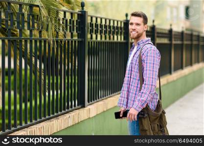 Young bearded man standing in urban background. Lifestyle concep. Young bearded man standing in urban background. Traveler wearing casual clothes. Lifestyle concept.