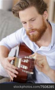 young bearded man tuning his guitar