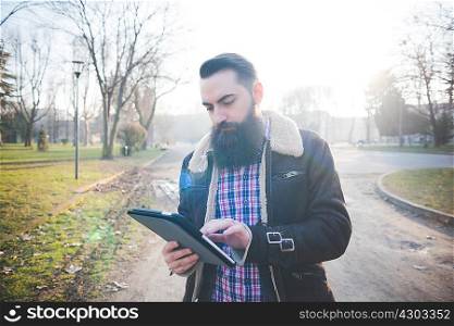 Young bearded man using digital tablet in park