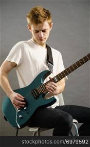 Young bearded man with electric guitar. Adult person is holding instrument and playing. Hobby, music concept, on grey. Young man playing electric guitar
