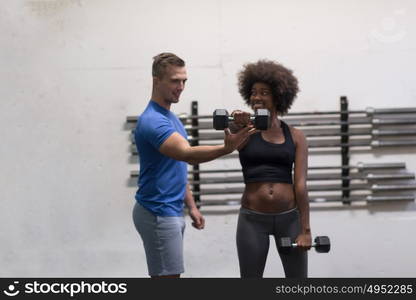 young beautiful African American woman doing bicep curls with fitness trainer in a gym