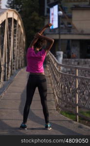young beautiful African American woman doing warming up and stretching before the morning run with the sunrise in the background