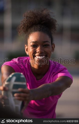 young beautiful African American woman doing warming up and stretching with her leg raised to the bridge before the morning run with the sunrise in the background
