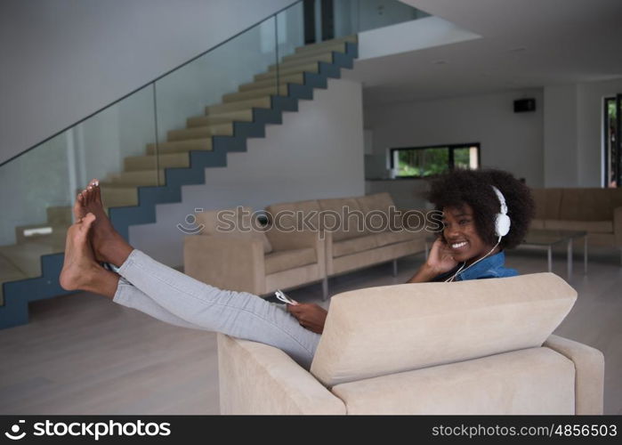 young beautiful African American woman enjoys listening to music with headphones and tablet in your armchair in her luxury home