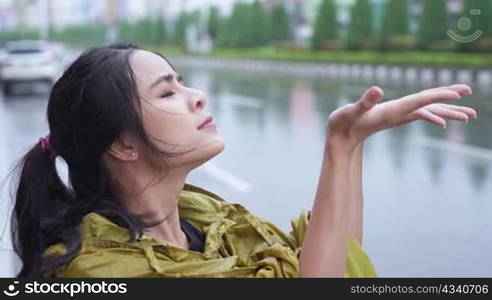 young beautiful asian female put on the hoody of yellow raincoat after using hands catching falling rains, rainy season weather, stormy sorrow, unlucky days, bad luck, urban street on the back ground