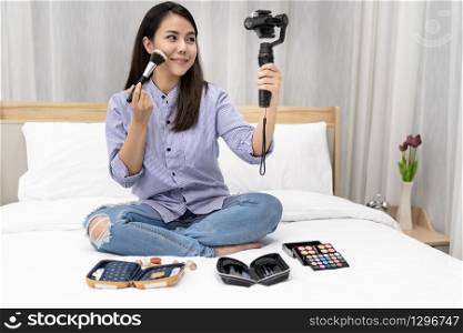 Young beautiful Asian woman beauty vlogger blogger recording live how to make up tutorial to share on social media using Gimbal Stabilizer on mobile phone. Use for vlog social media influencer concept