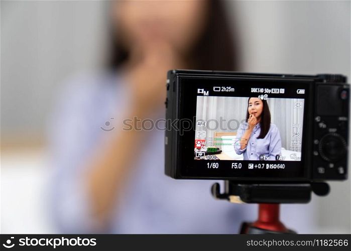 Young beautiful Asian woman beauty vlogger or blogger recording live how to make up tutorial to share on social media using digital camera on table tripod. Using for vlog social media influencer concept. Focus on camera.