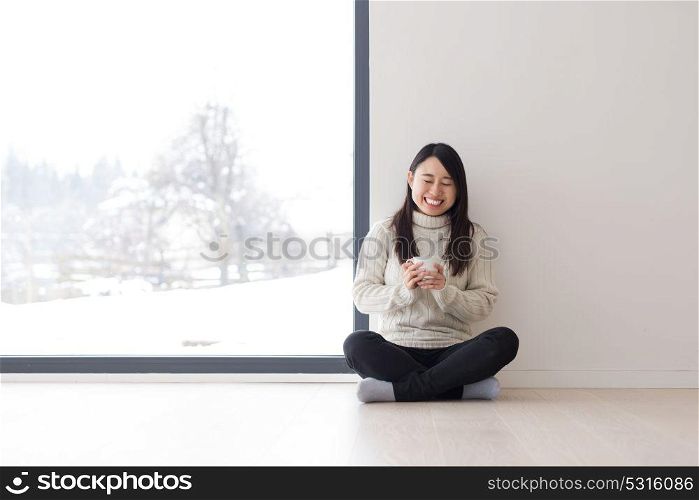 young beautiful asian woman enjoying morning coffee on the floor near window at cold winter day