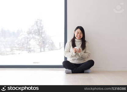 young beautiful asian woman enjoying morning coffee on the floor near window at cold winter day