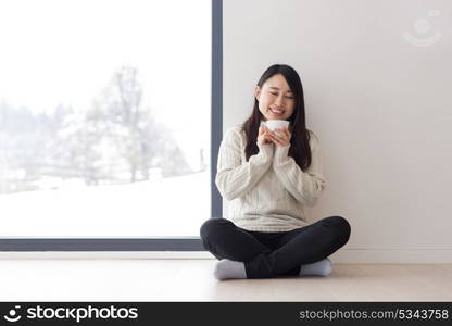 young beautiful asian woman enjoying morning coffee on the floor near window at cold winter day