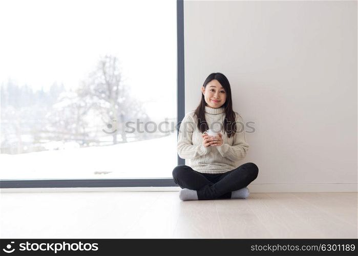 young beautiful asian woman enjoying morning coffee on the floor near window at cold winter day