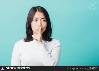 Young beautiful Asian woman holding index finger on her mouth lips, Portrait female hush silence, studio shot isolated on a blue background, Gesture of shhh