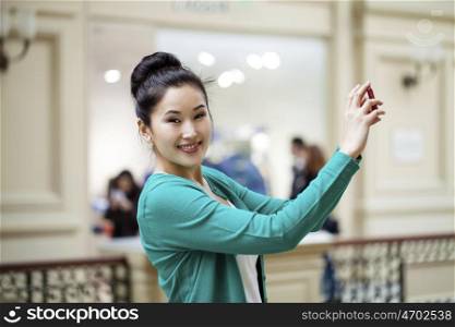 Young beautiful asian woman tourist taking pictures on mobile phone in Moscow Shop