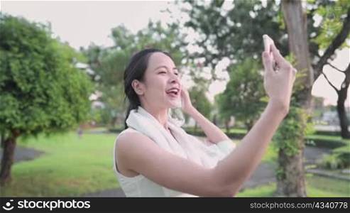 Young beautiful asian woman, video calling through smartphone during exercising at the park ,talking with friend telling stories, social distancing concept, distanced relationship, digital technology