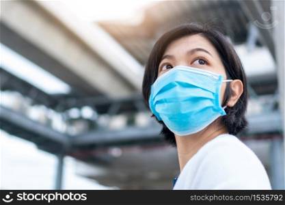 Young Beautiful Asian woman wearing blue surgical mask looking something in new normal life while pandemic covid-19 or coronavirus at outdoor
