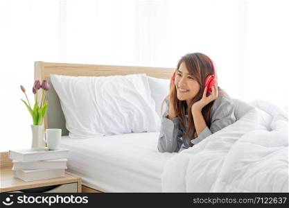 young beautiful asian women listen to music on the couch happily on the morning of the weekend. young Asian woman wakes up in the morning and listens to music before drinking coffee on the white bed in a hotel room.An Asian girl rested by lying down to listen to the red headphones on her bed.