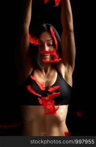young beautiful athletic girl in black clothes throws up red feathers, arms raised up, low key