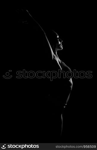 young beautiful athletic girl with muscles in a black bra bent the body back, arms raised up, contour silhouette, black and white toning
