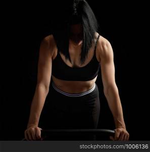 young beautiful athletic girl with muscles in a black bra is wrung out in her arms, doing fitness and sports, studio photo in a low key