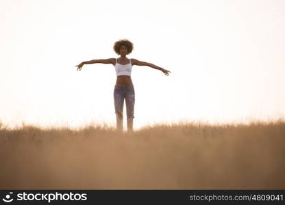 Young beautiful black girl laughs and dances outdoors in a meadow during sunset