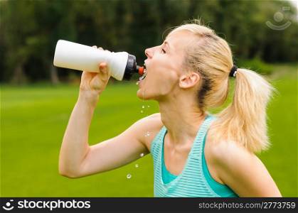Young beautiful blond woman drinking water at summer green park