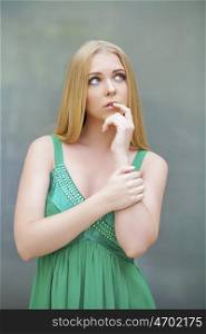 Young beautiful blonde girl thinking about something, indoor young woman in green dress