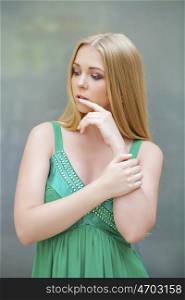 Young beautiful blonde girl thinking about something, indoor young woman in green dress