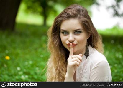 Young beautiful blonde woman has put forefinger to lips as sign of silence, outdoors