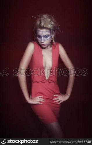 Young beautiful blonde woman in a red dress and veil on dark background